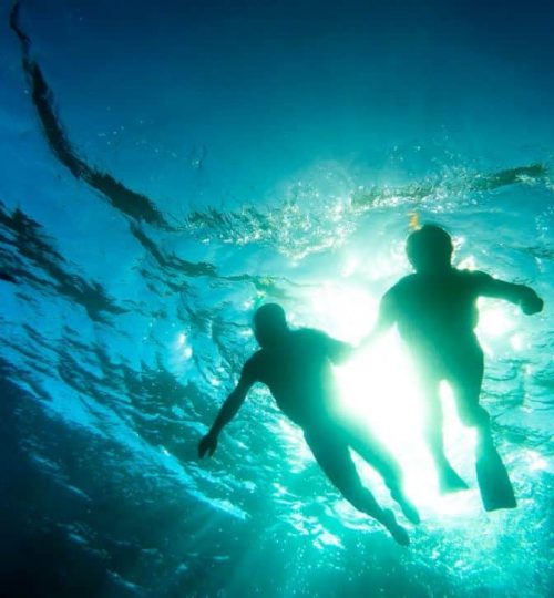 Silhouette of senior couple swimming together in tropical sea -